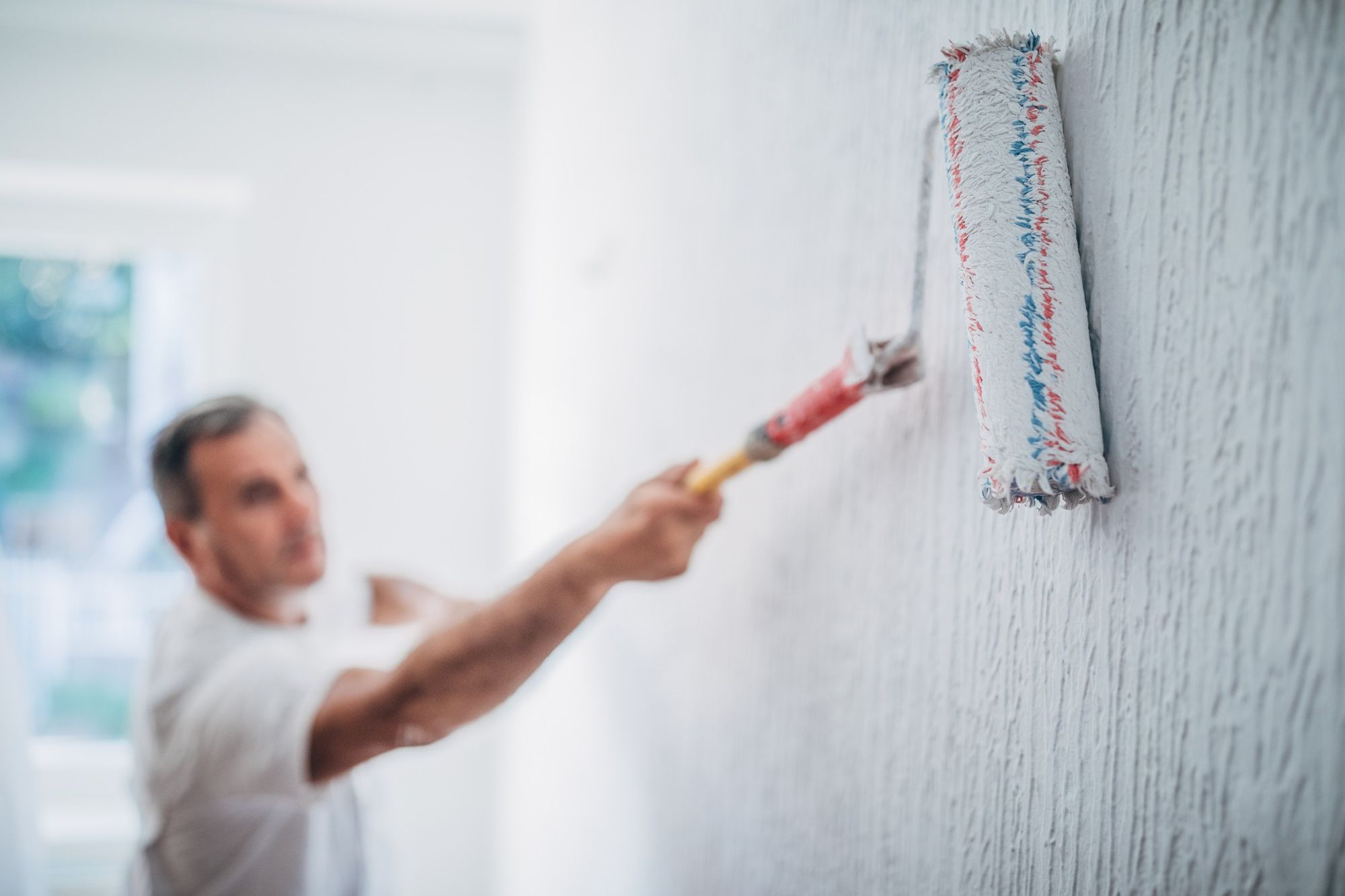 Homem com uma camiseta branca pintando a parede de branco