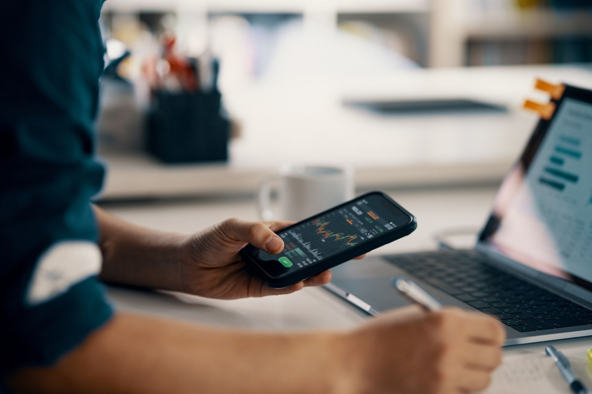 Um homem segurando um celular com um aplicativo de bolsa de valores aberto