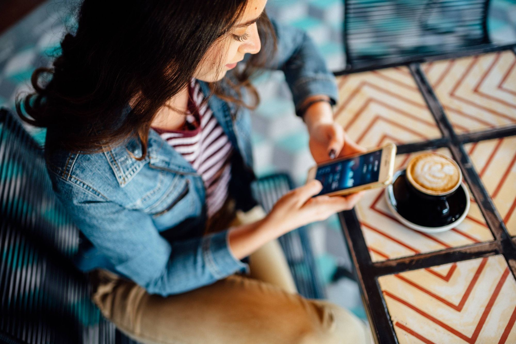 Mulher sentada com um café na mesa e segurando um iPhone